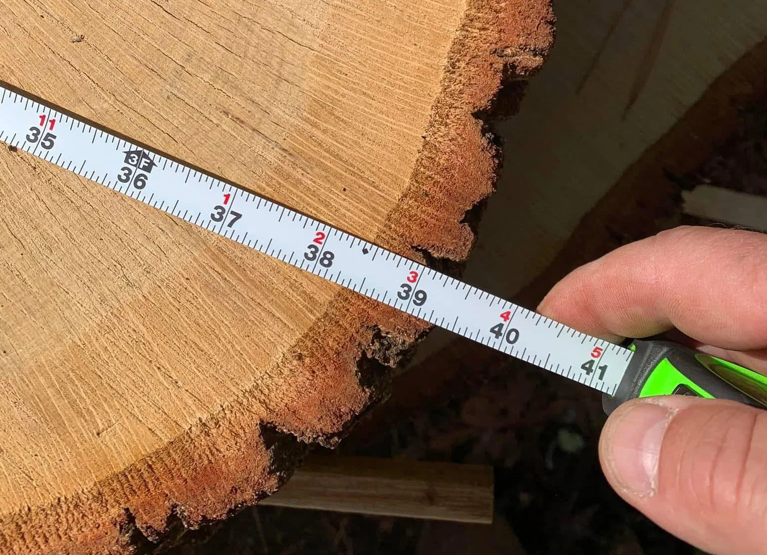 A person holding a measuring tape across the surface of a wood log